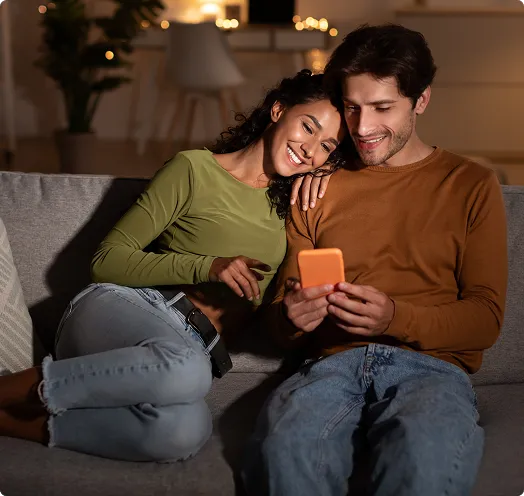 Couple sitting on a couch looking at a phone screen - First time home owners
