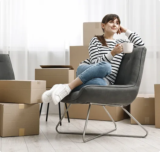 Person sitting on a chair with a cup of coffee surrounded by moving boxes